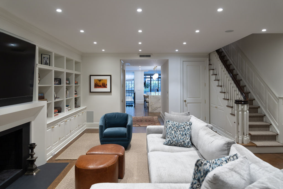 Living room with built-in shelves, fireplace, blue armchair, and a staircase. Light-colored walls and flooring.