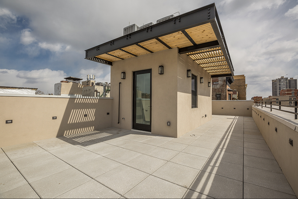 Rooftop terrace with tan walls, gray tiled floor, and a canopy. Sunny day.