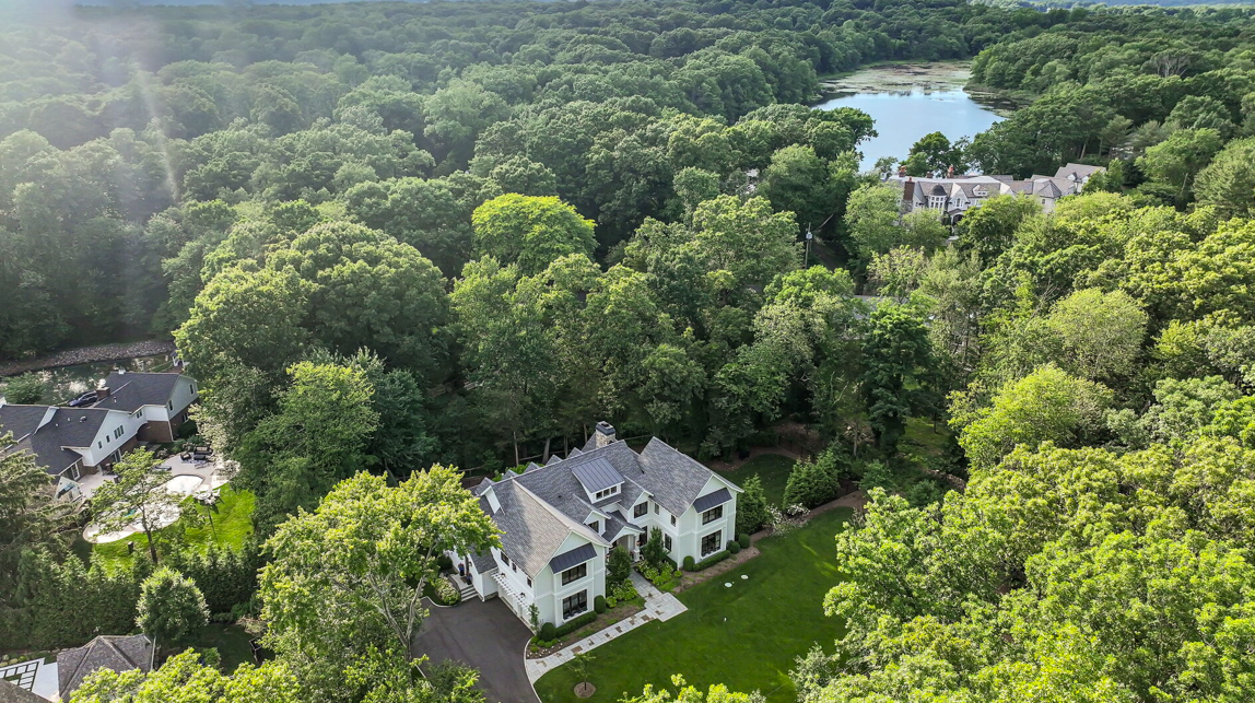 Aerial view of a large white house surrounded by green trees and a lake in the background.