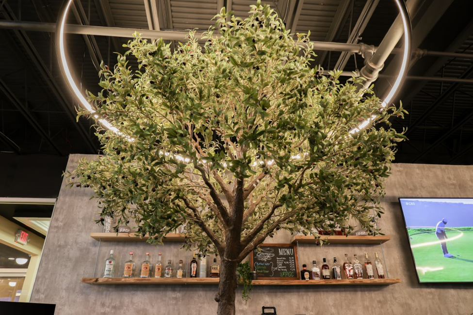 Tree-shaped structure with shelves of liquor bottles against a textured wall, with a television playing golf and a circular light fixture.