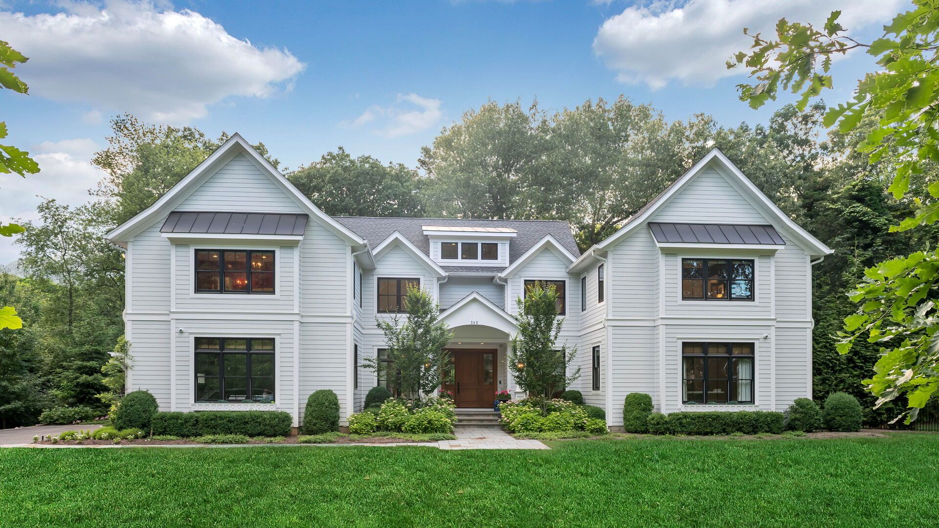 White two-story house with dark trim and a green lawn under a partly cloudy sky.