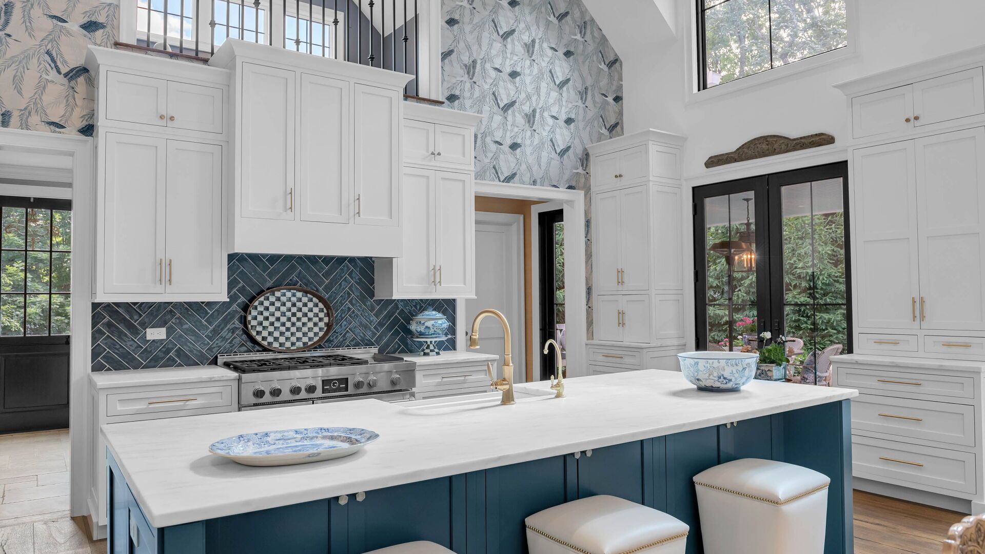 A modern kitchen with a blue island and white cabinets. Blue and white patterned wallpaper accents the walls.