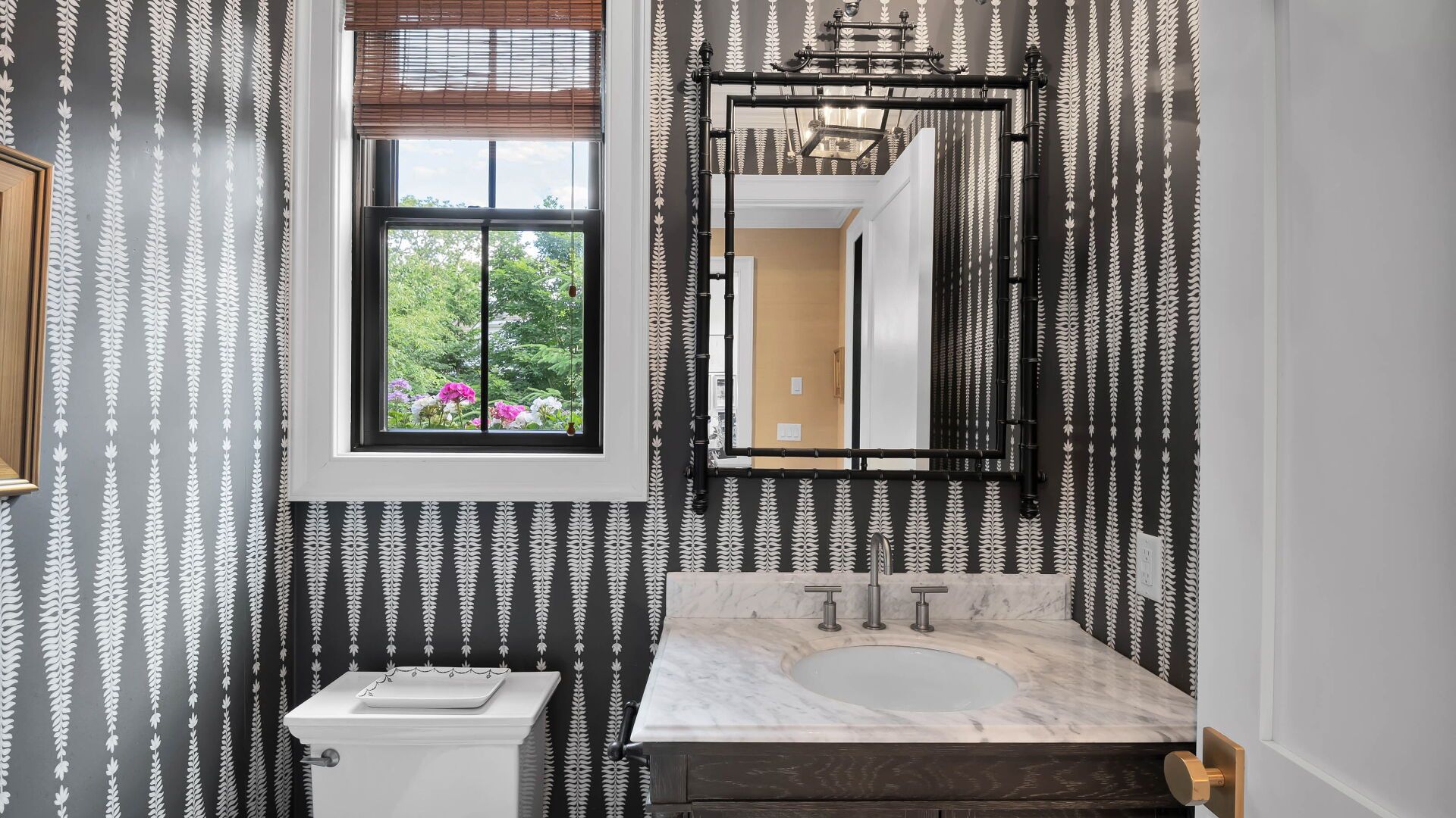 Powder room with patterned wallpaper, marble vanity, and decorative mirror.