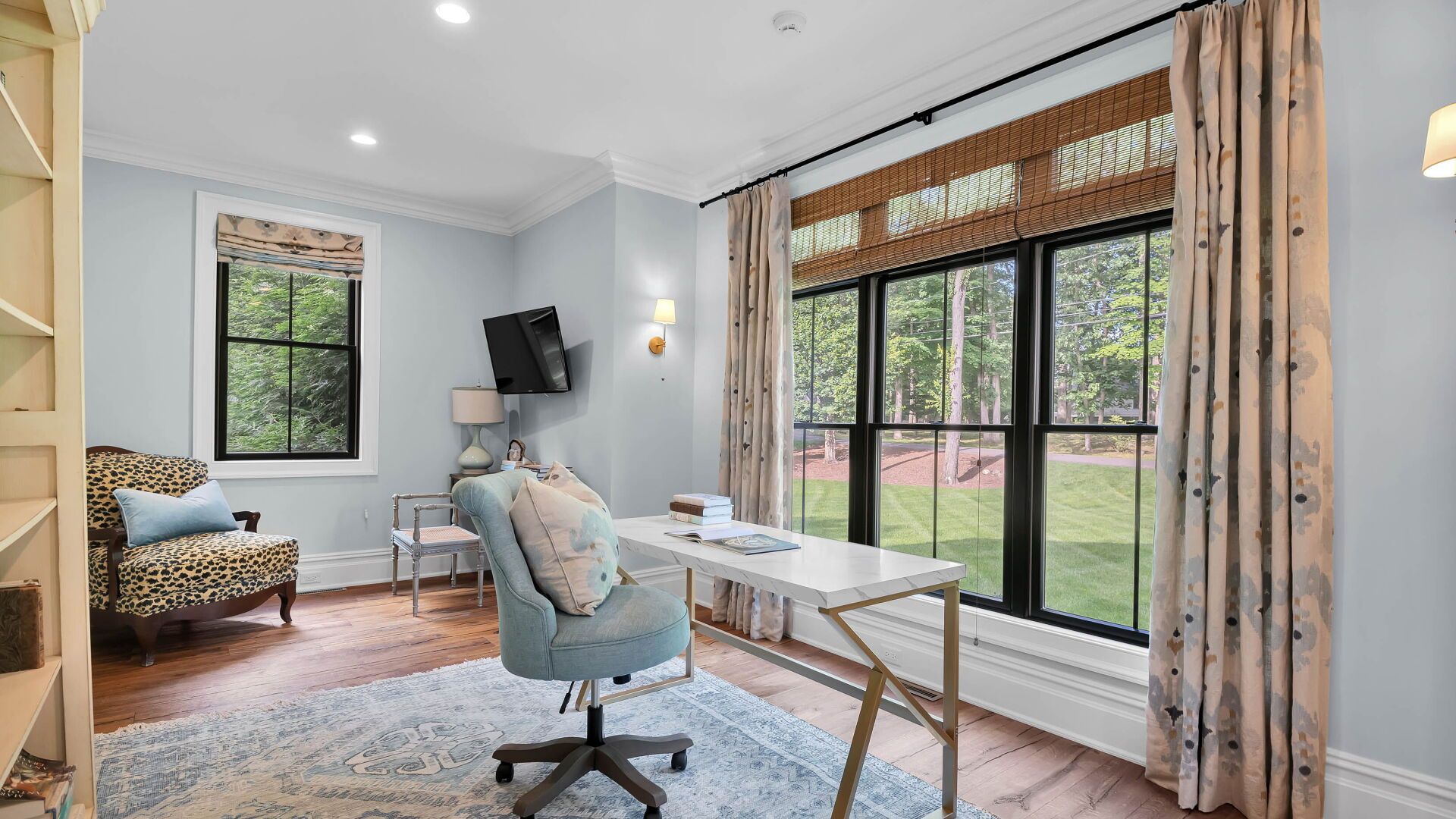 Home office with desk, chair, window, light blue walls, and patterned curtains.