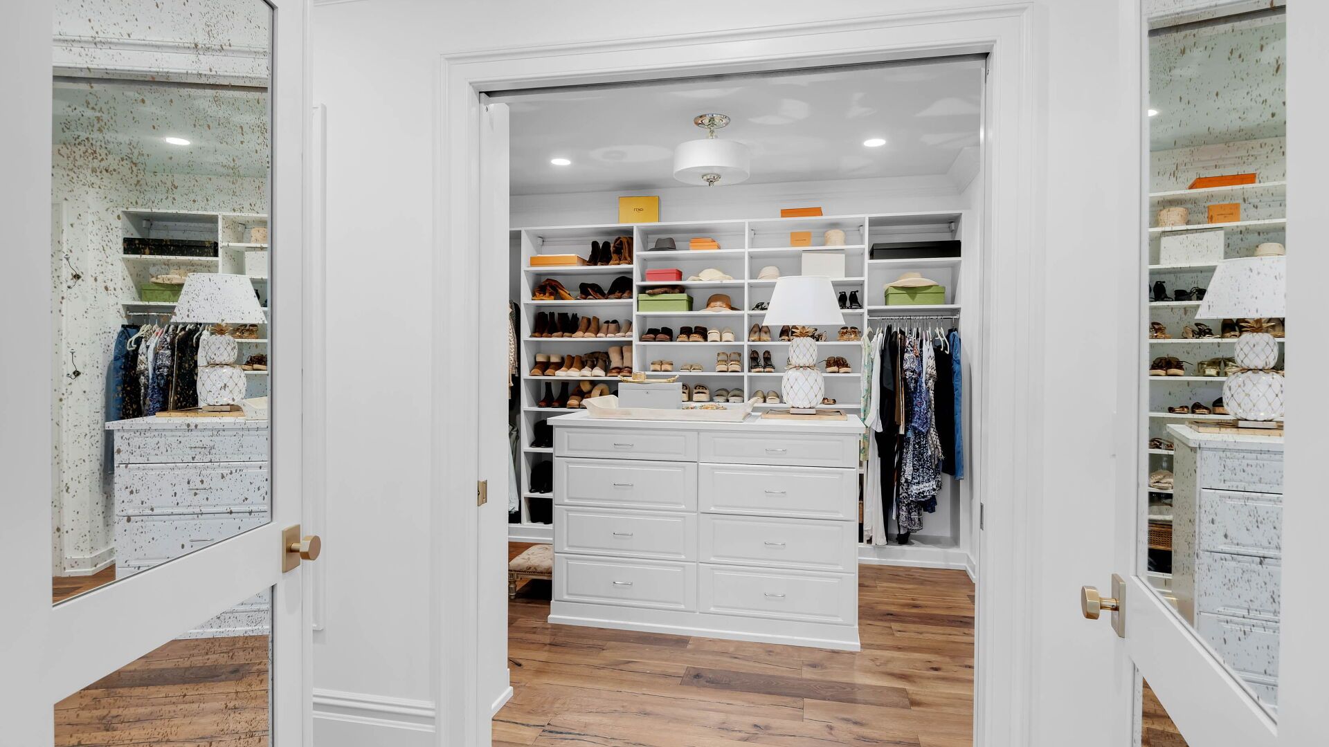 Walk-in closet with white shelves and drawers, wooden floors, and a center island.