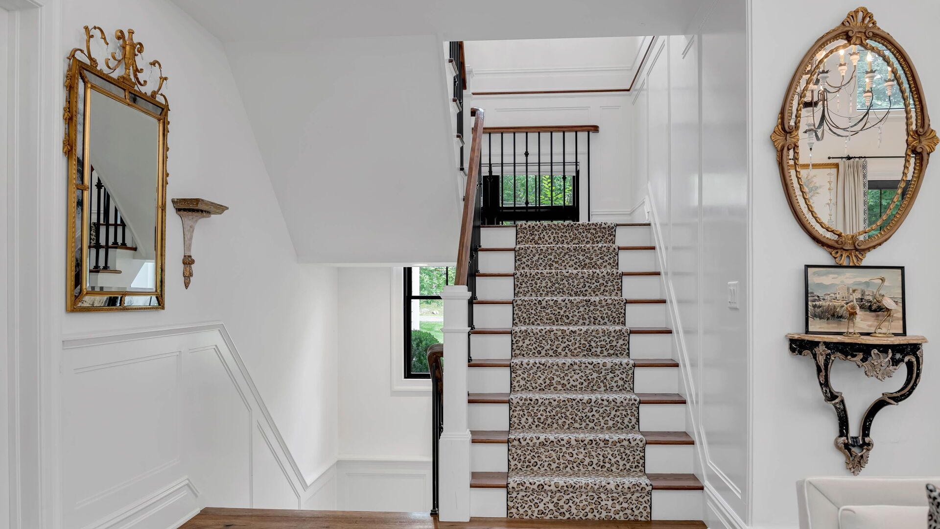 Elegant white staircase with patterned carpet runner, gold mirrors, and decorative wall shelves.