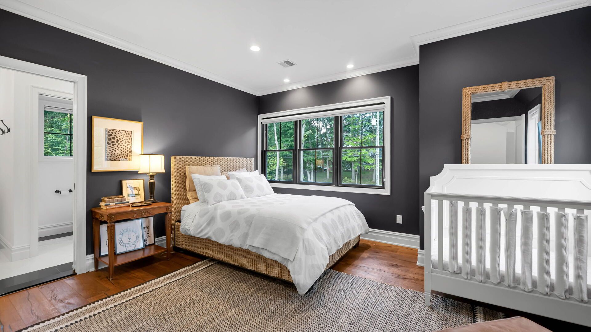 Bedroom with a gray wall, a wooden bed, a white crib, and a large window.