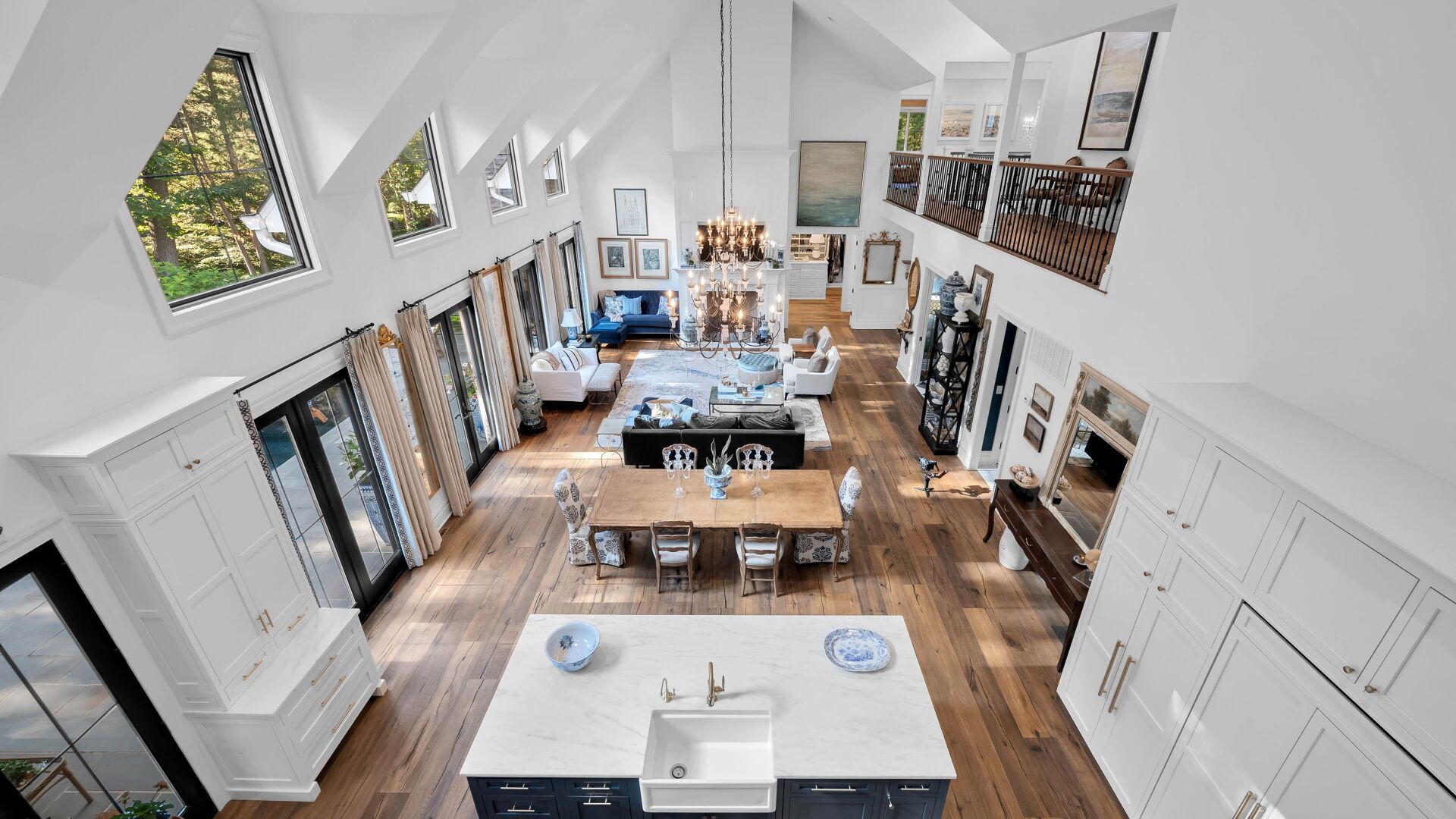 High-angle view of a bright, open-plan living and dining area with tall ceilings, windows, and wooden floors.