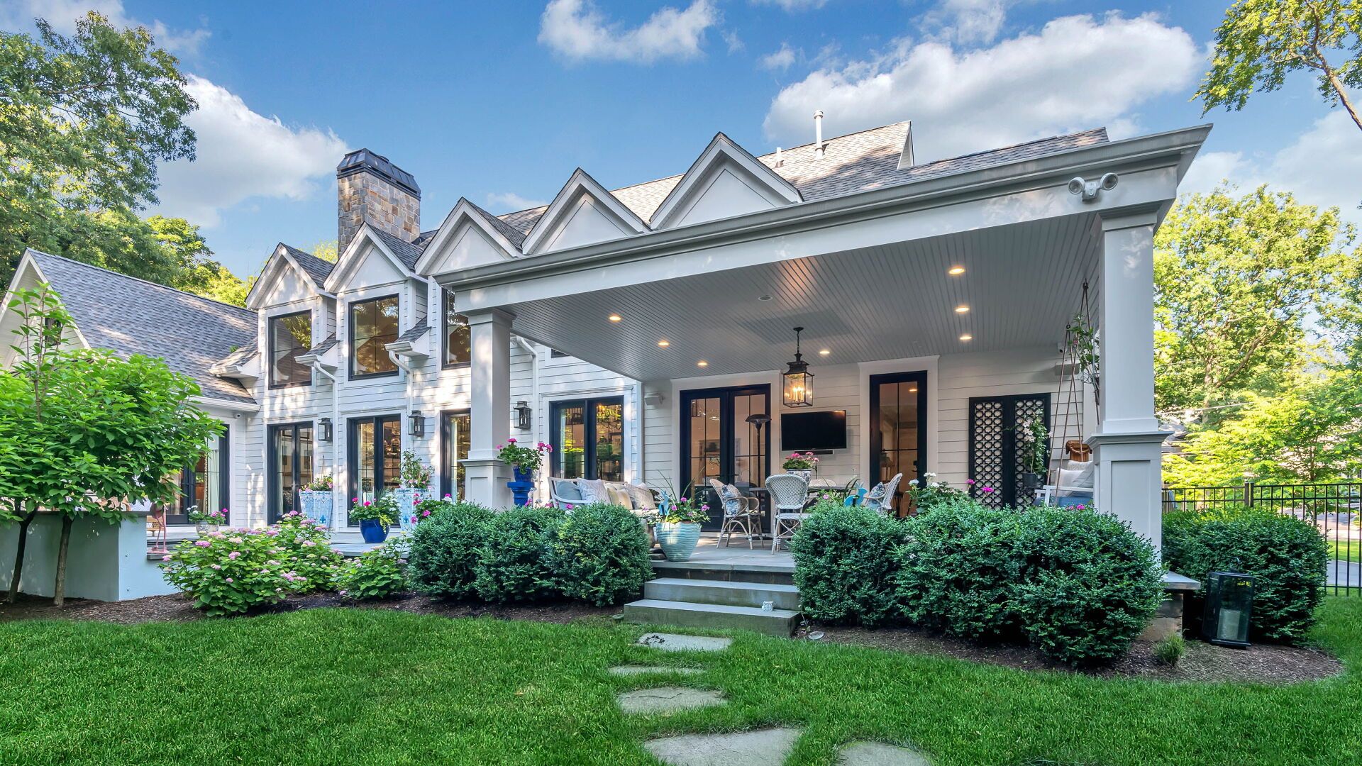 White house with covered patio, black doors, and lush green landscaping.