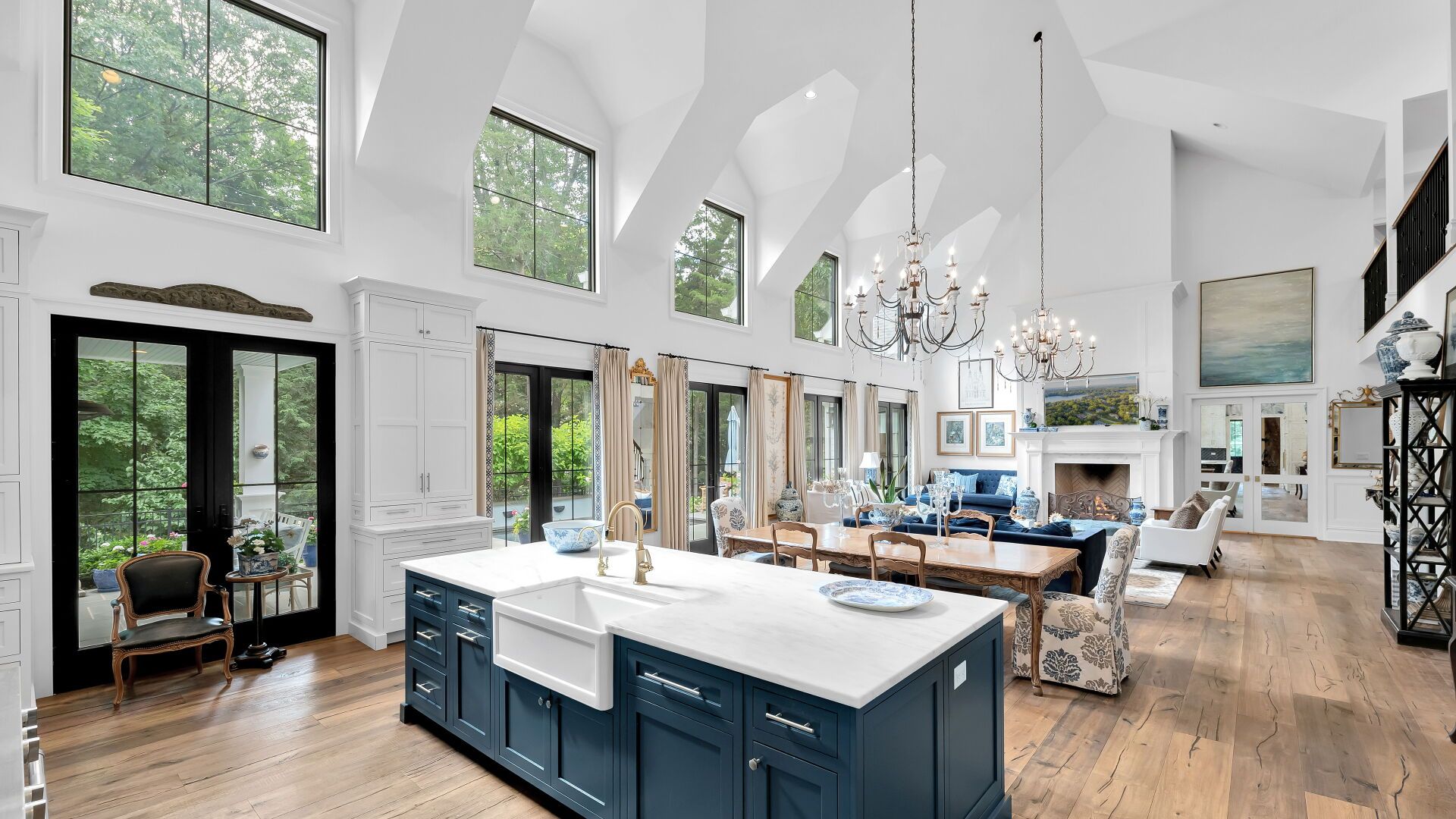 Spacious, bright kitchen with blue island, farmhouse sink, and high ceilings, open to living and dining areas.