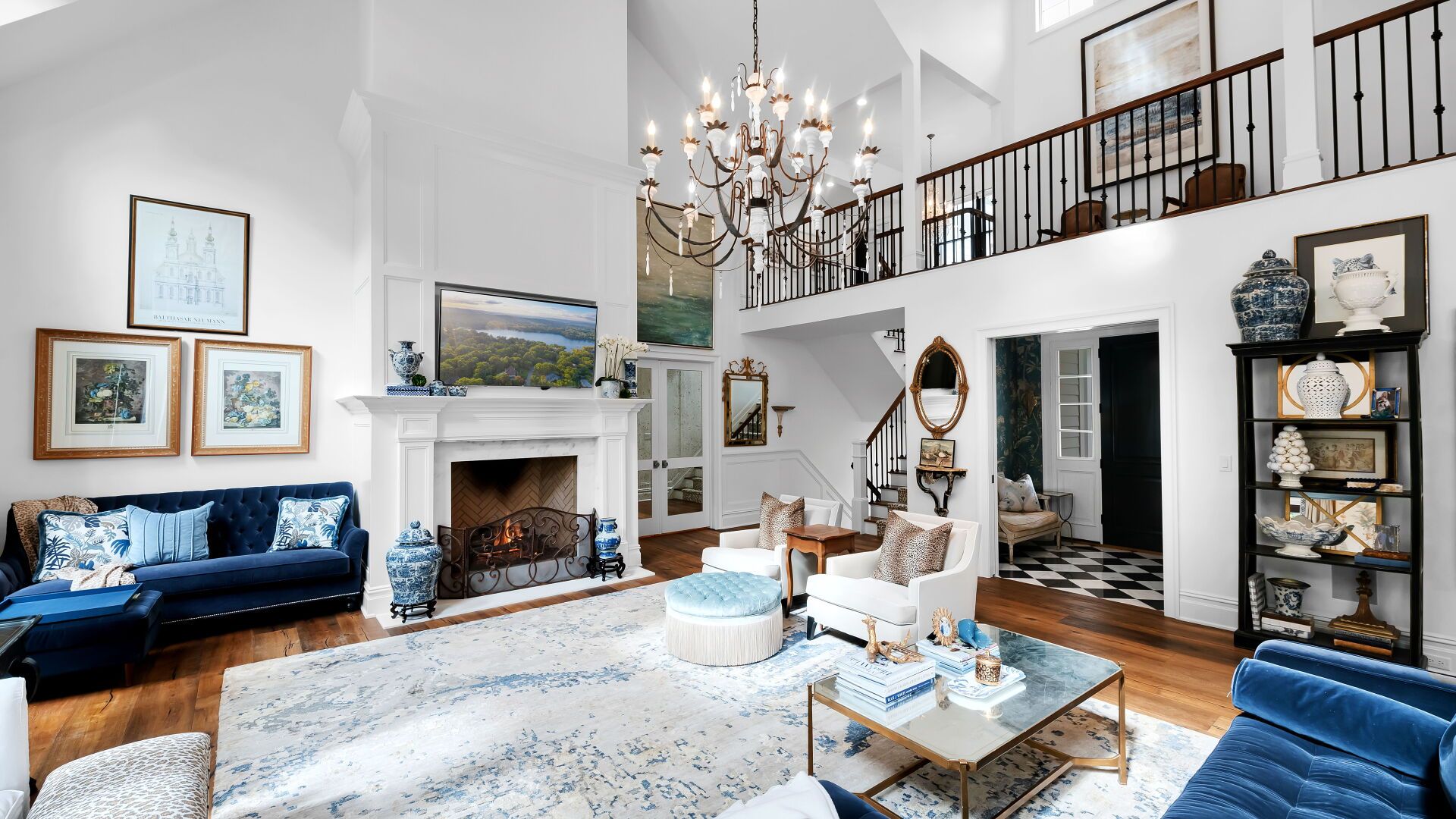 Elegant living room with a two-story ceiling, chandelier, blue velvet sofa, and fireplace.