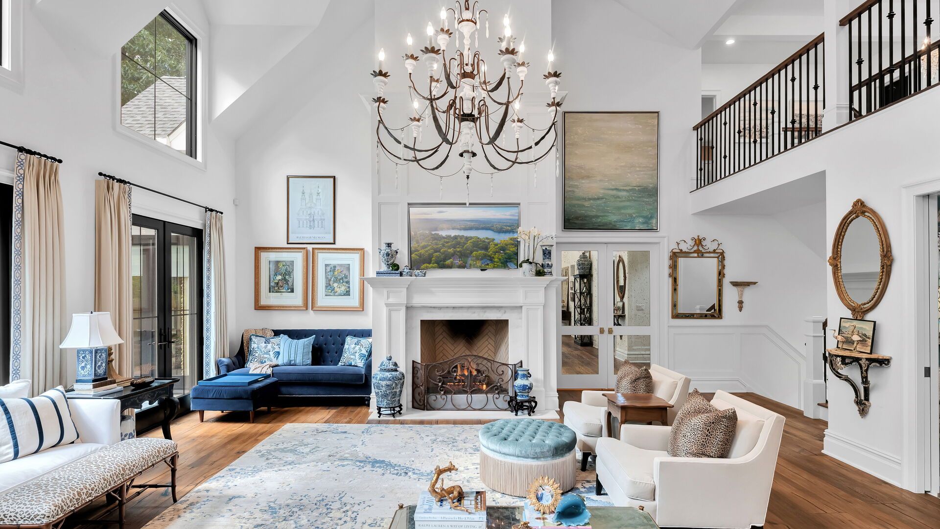 Spacious, bright living room with white walls, fireplace, chandelier, and various furniture, including a blue sofa.