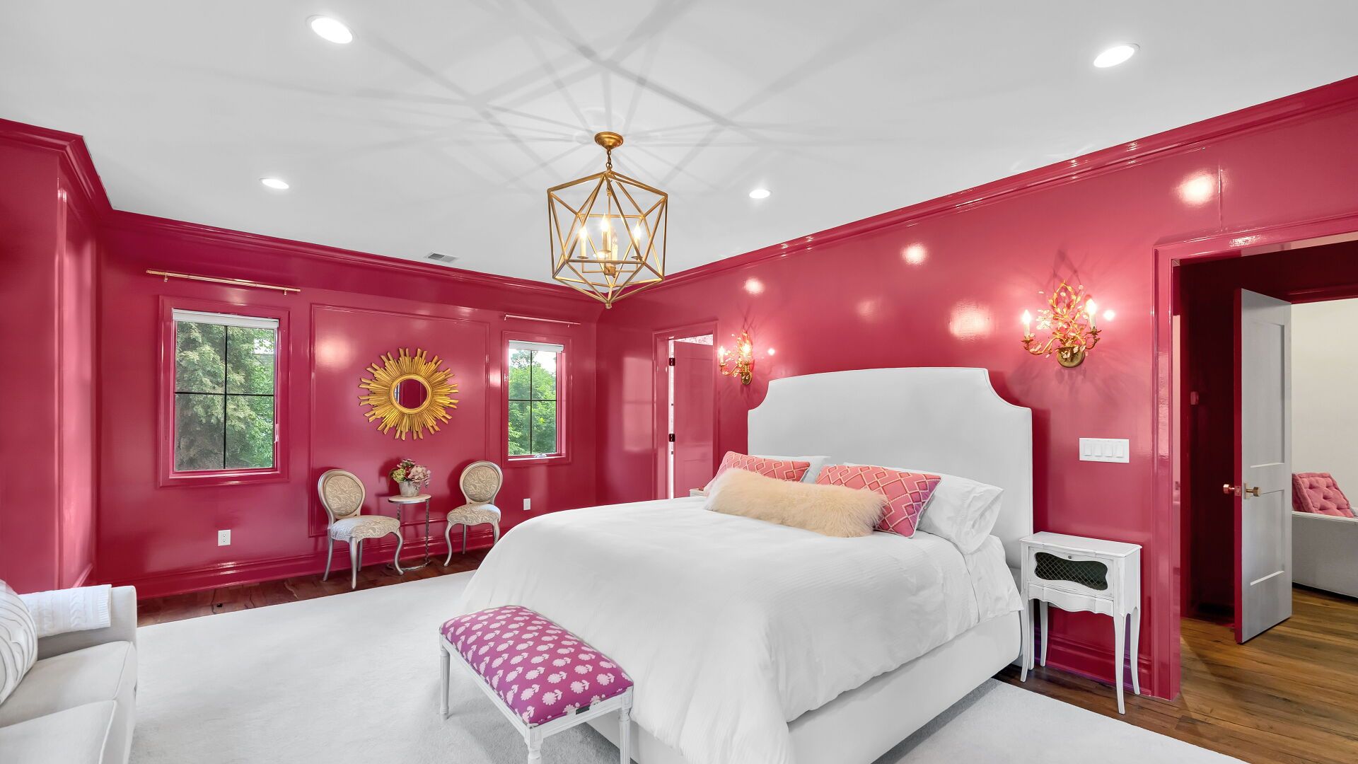 Luxurious bedroom with magenta walls, white bed, gold accents, and geometric chandelier.
