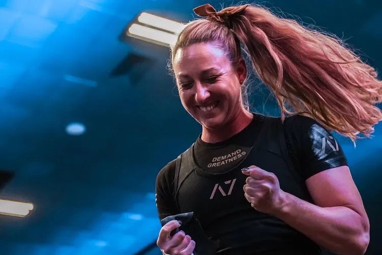 Smiling athlete in black shirt clenches fists under blue stage lighting