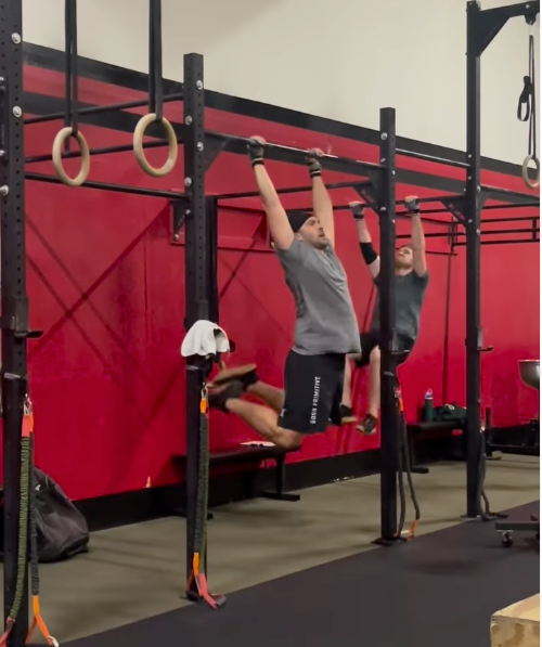 Two people doing pull-ups on a black rig in a red gym