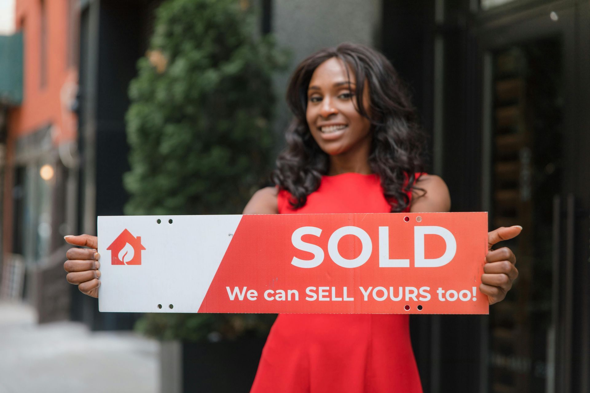 A woman in a red dress is holding a sold sign.