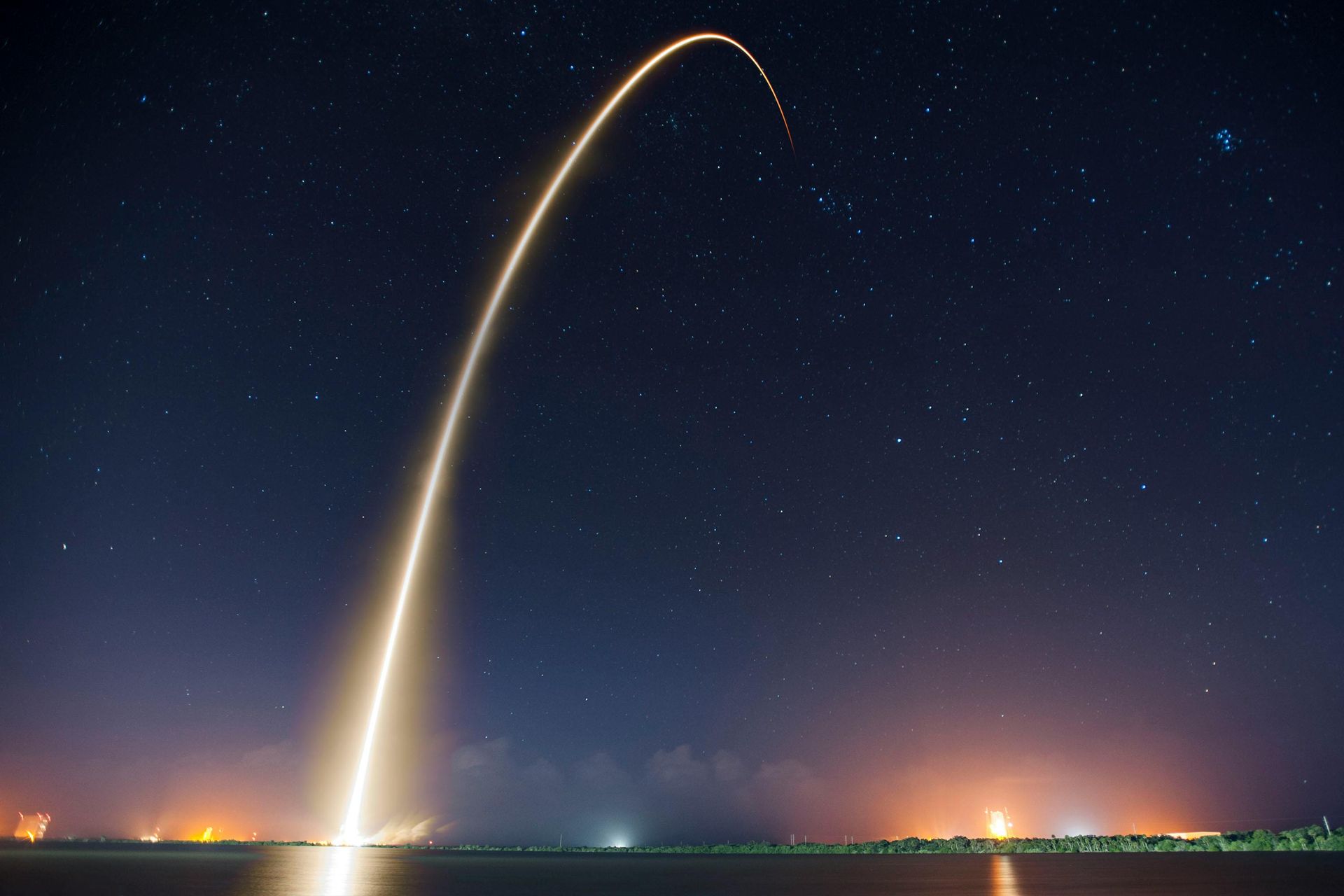 A rocket is flying through the night sky over a body of water.