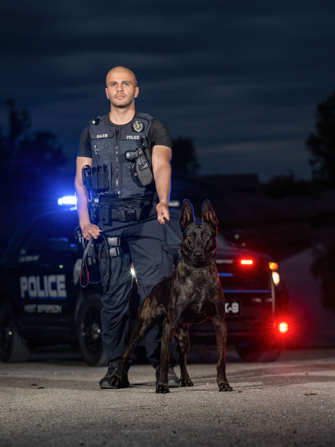 A police officer and his dog are posing for a picture in front of a police car.