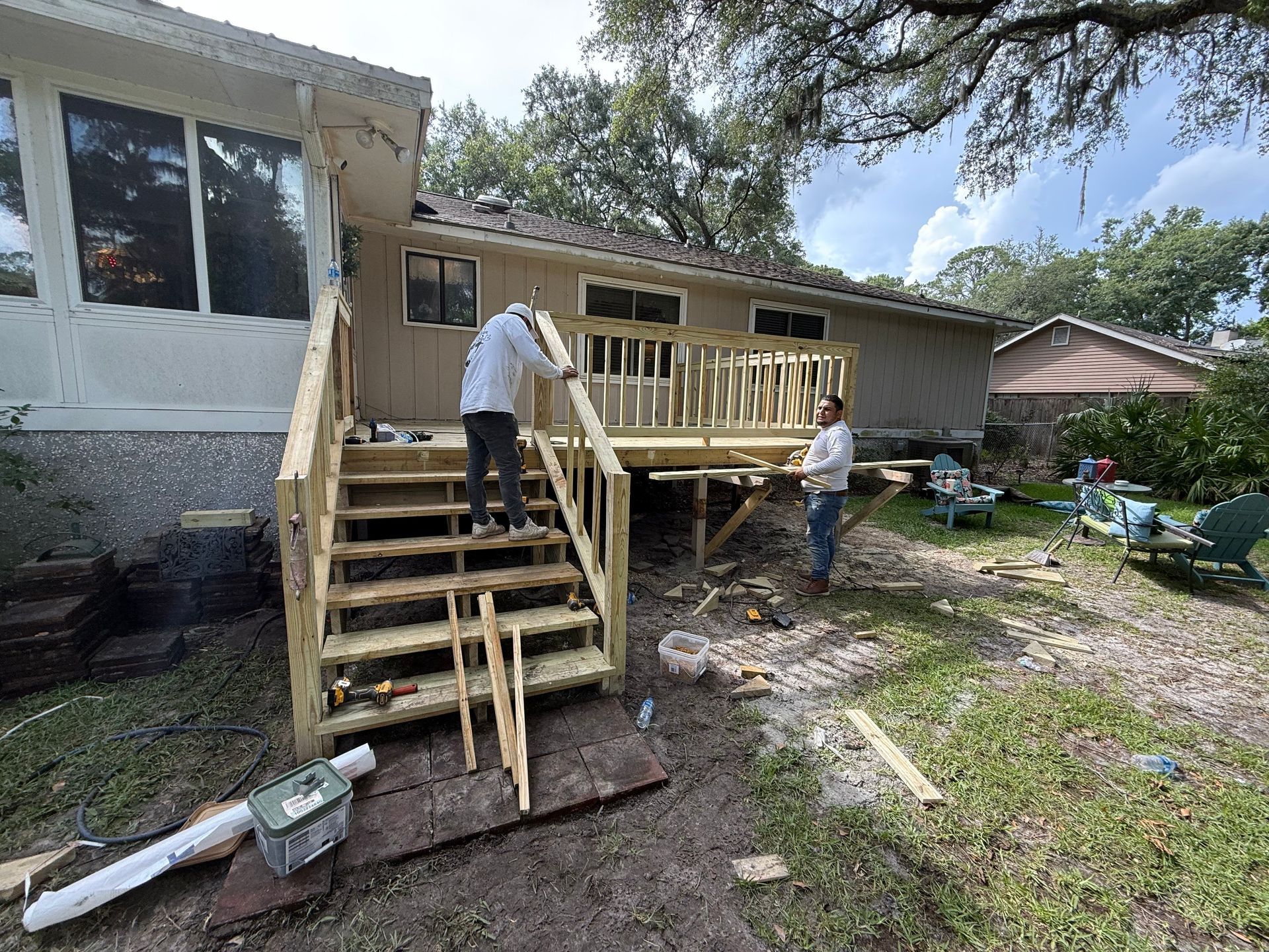 Two people building a wooden deck and stairs next to a house.