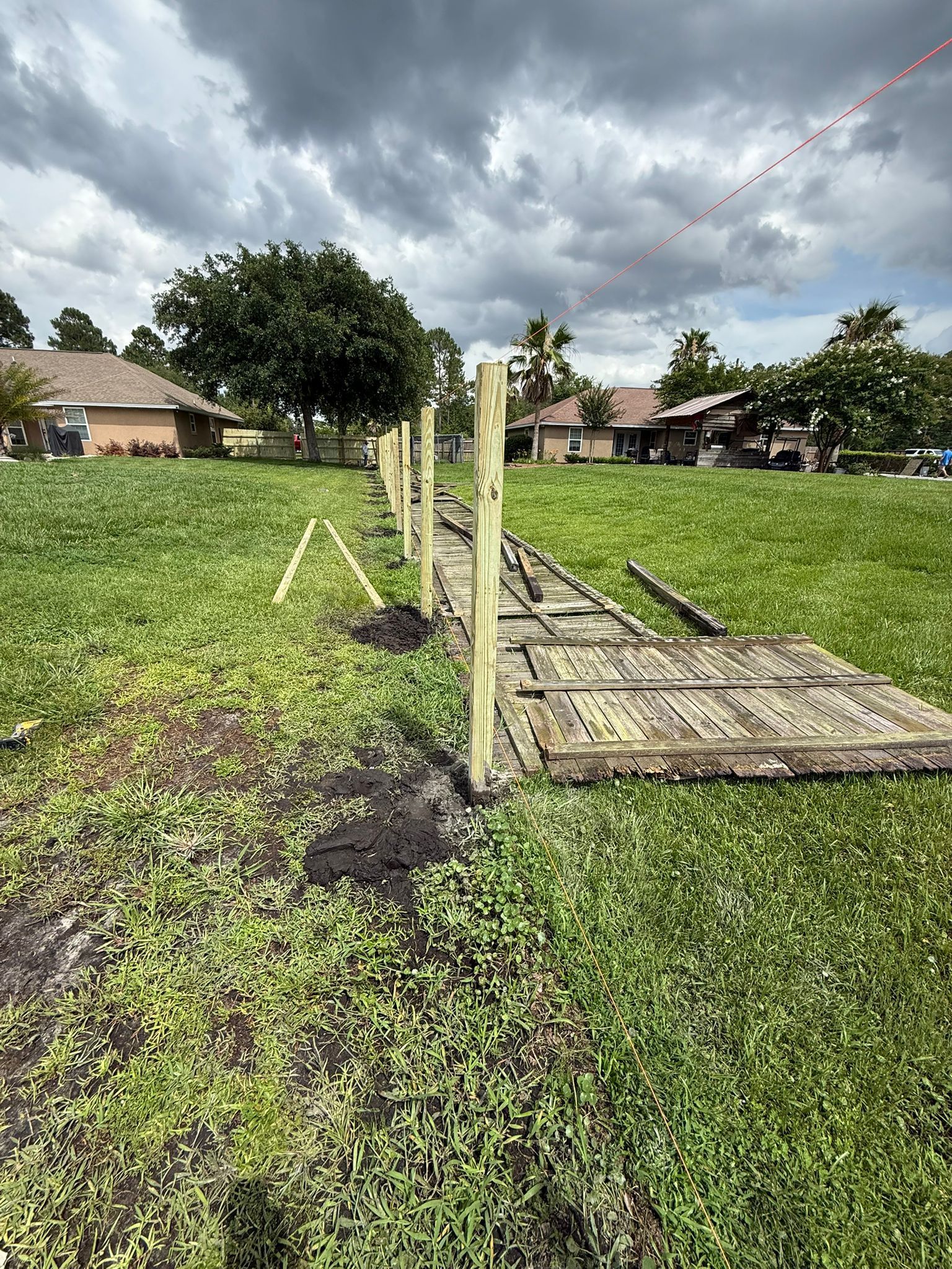 Partially built wooden fence in grassy yard under a cloudy sky.