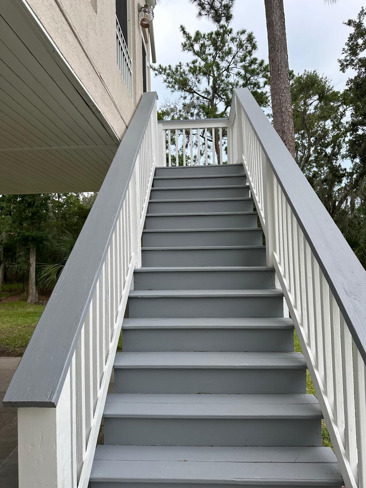 Outdoor staircase leading up to a building, painted gray and white, surrounded by greenery.