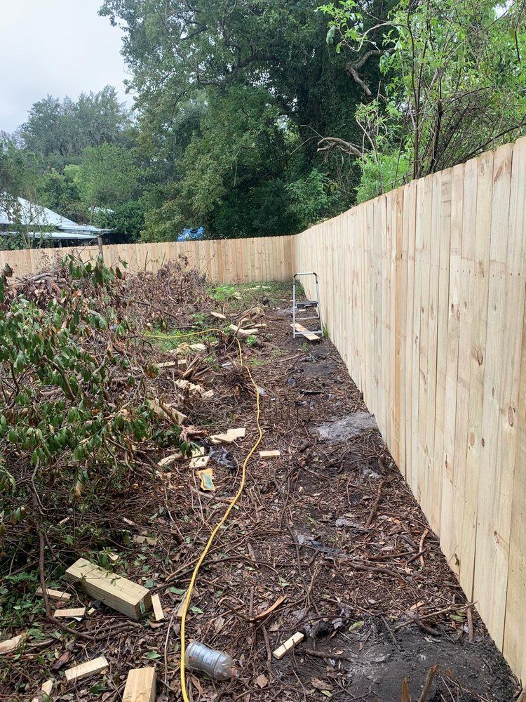 A new wooden fence bordering a muddy yard filled with debris and construction materials.