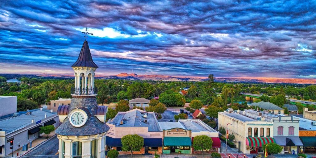 Town square with a clock tower at sunset under a colorful cloudy sky