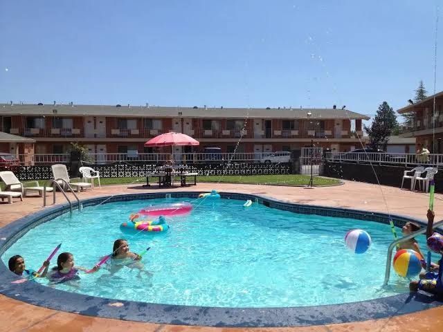 Motel pool with children swimming and floating toys under a red umbrella on a sunny day