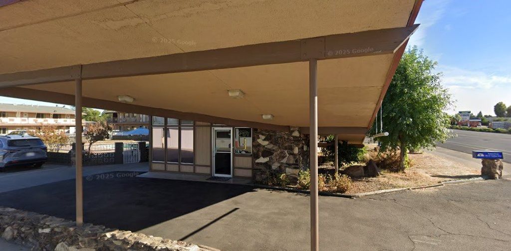 Covered outdoor walkway beside a storefront, with parked cars and a dry, open lot in the background.