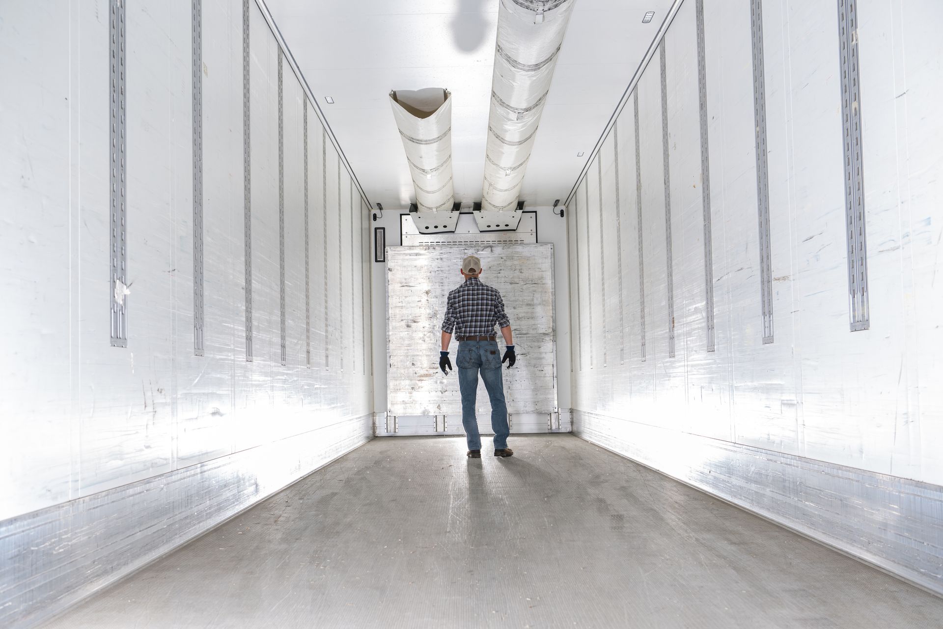 Worker standing inside the empty interior of a refrigerated trailer near the ceiling cooling vent