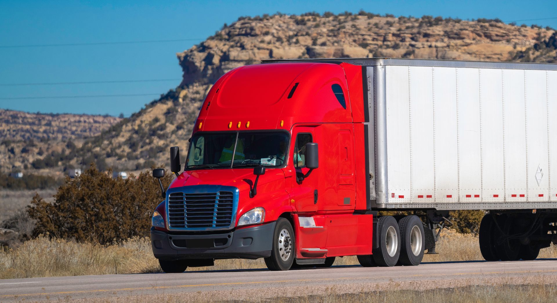 Red semi-truck hauling a large box trailer along a highway.