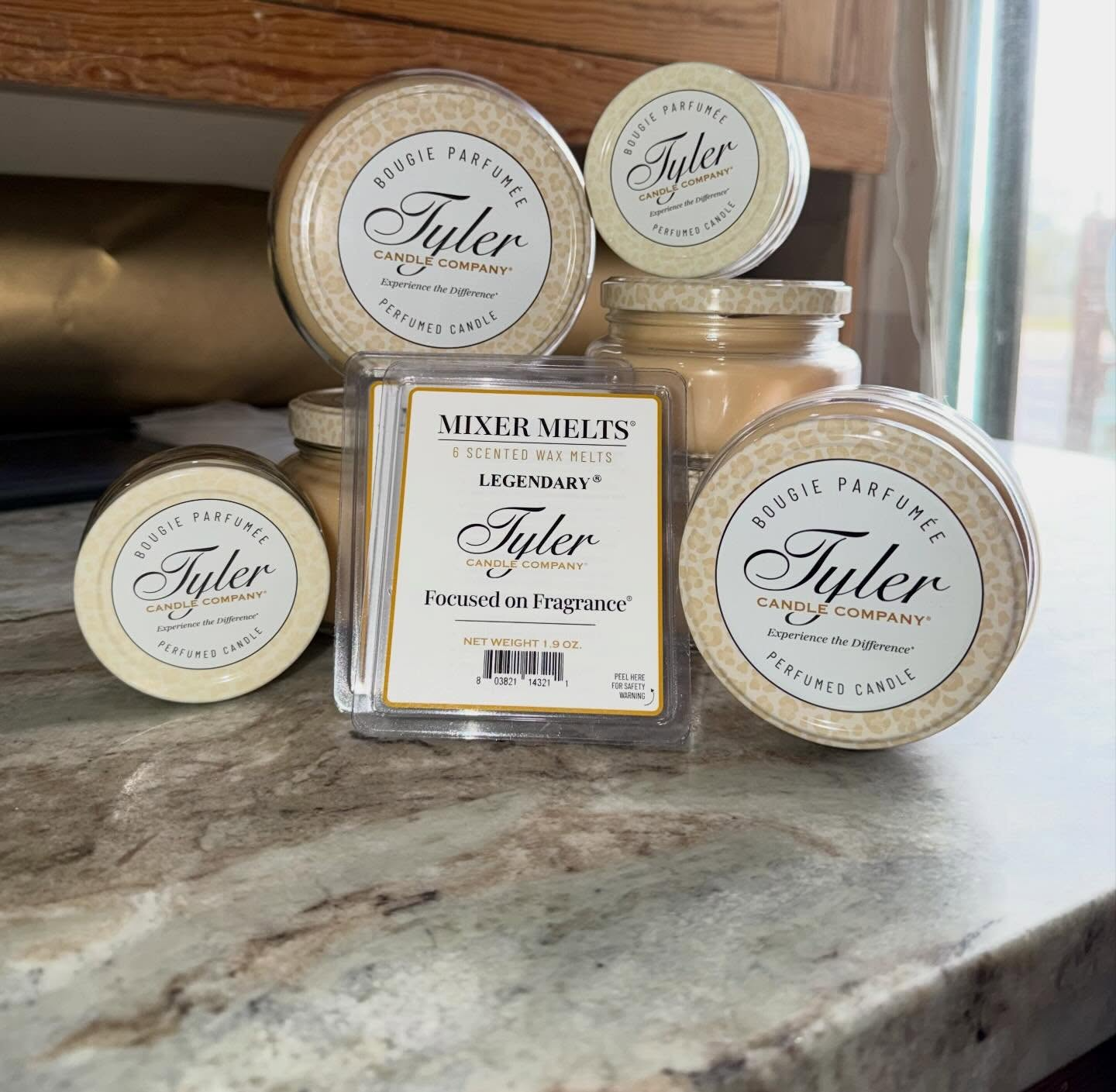 Assorted Tyler candle jars and a square Tyler soap jar on a marble countertop near a window
