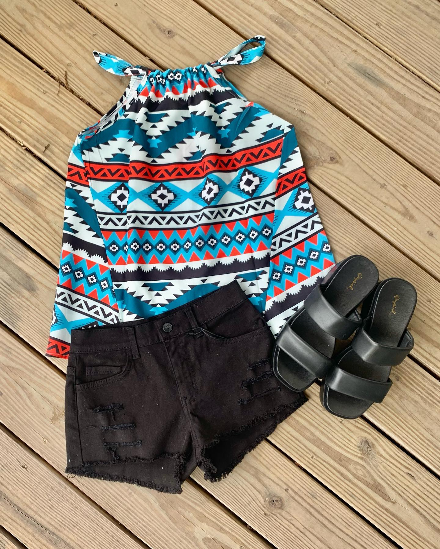 Colorful patterned romper, black shorts, and black shoes arranged on a wooden deck.