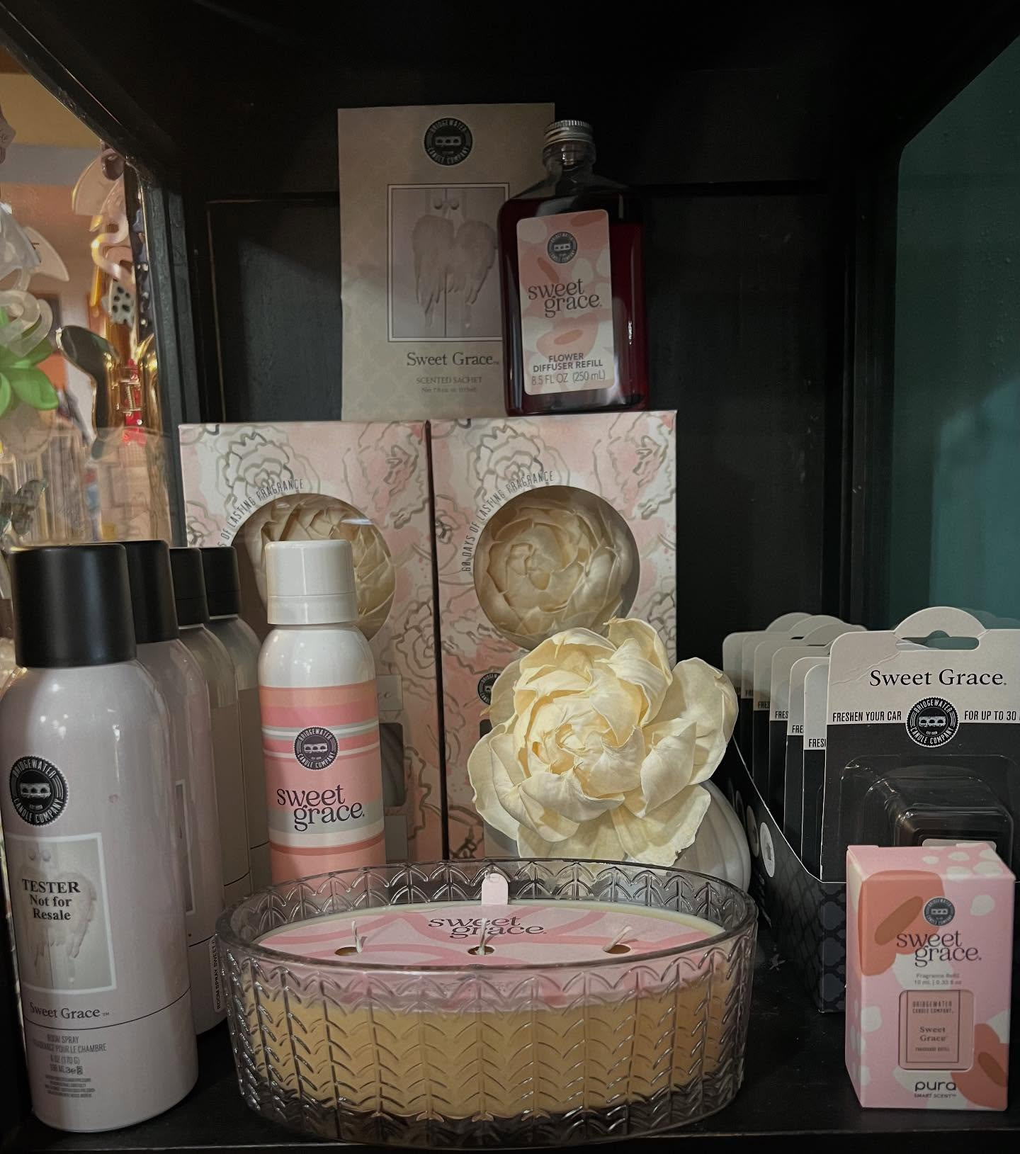 Gift set display with pink and cream bath products, candle, and decorative flower arrangement on a shelf