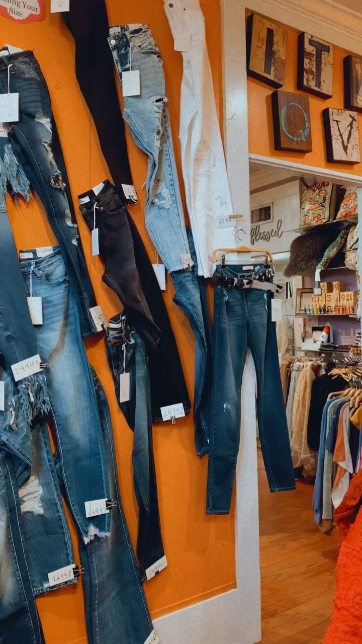 Jeans displayed on orange wall in a clothing store, with folded denim and framed decor nearby