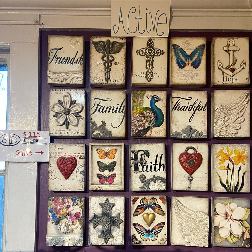 Wall of framed inspirational art and religious motifs with butterflies, hearts, flowers