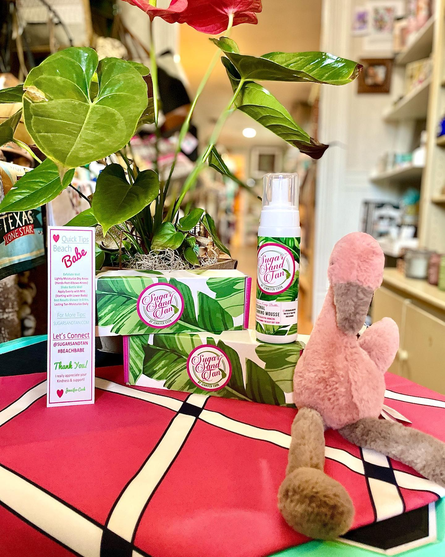 Pink plush bunny beside product boxes and bottles on a red patterned table in a shop.
