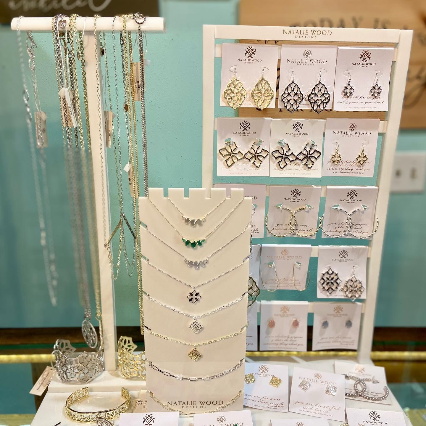 Jewelry display with ornate necklaces and earrings on cream stands against a teal background