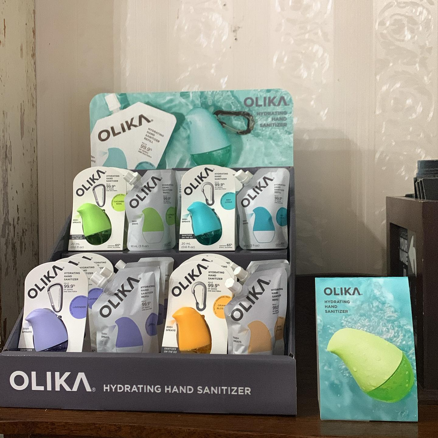 OLIKA hydrating hand sanitizer display with assorted pastel-colored bottles and a leaf image