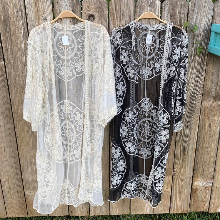 Two lace cover-ups hanging on a wooden fence, one white and one black.