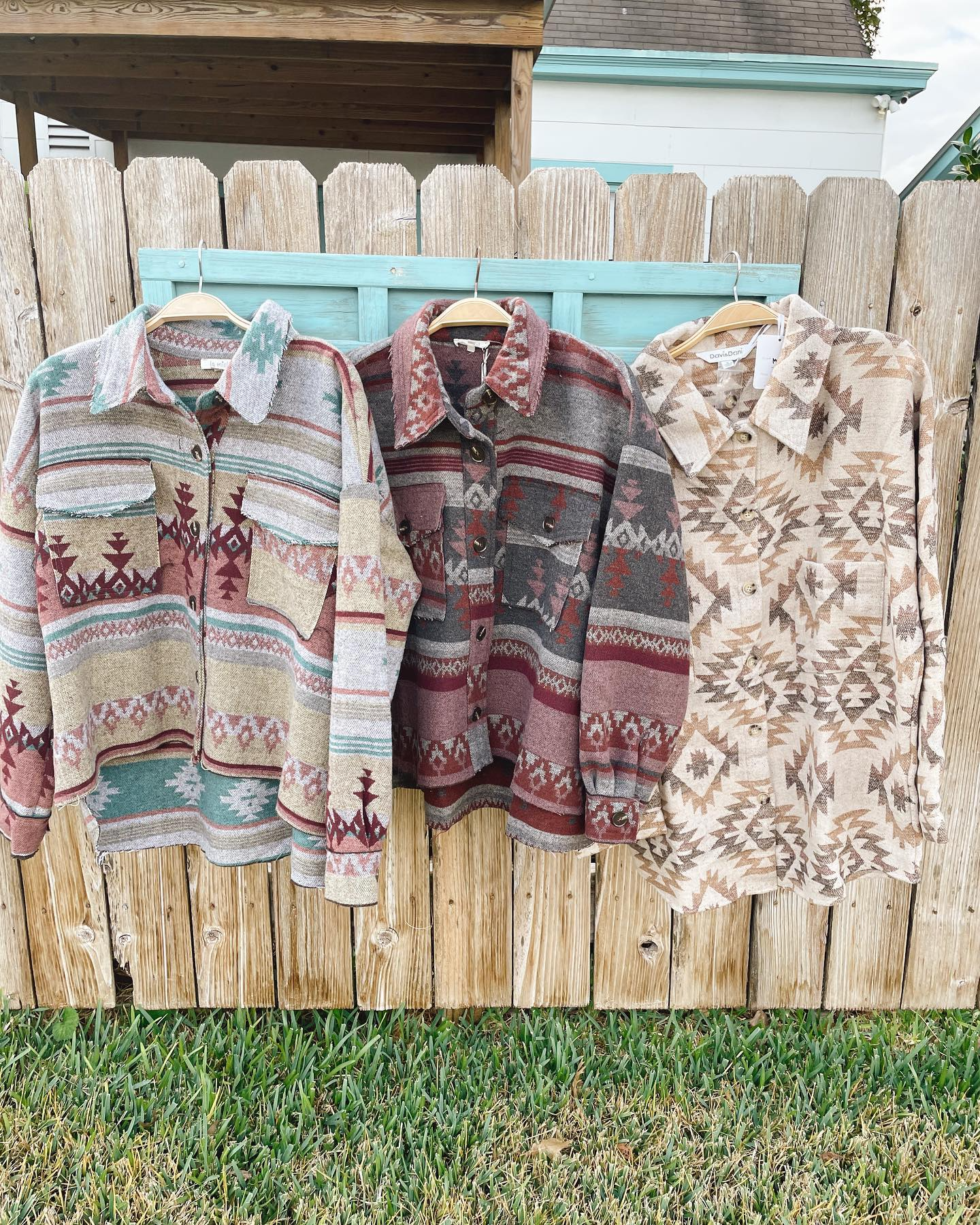 Three patterned jackets hanging on a wooden fence outdoors.