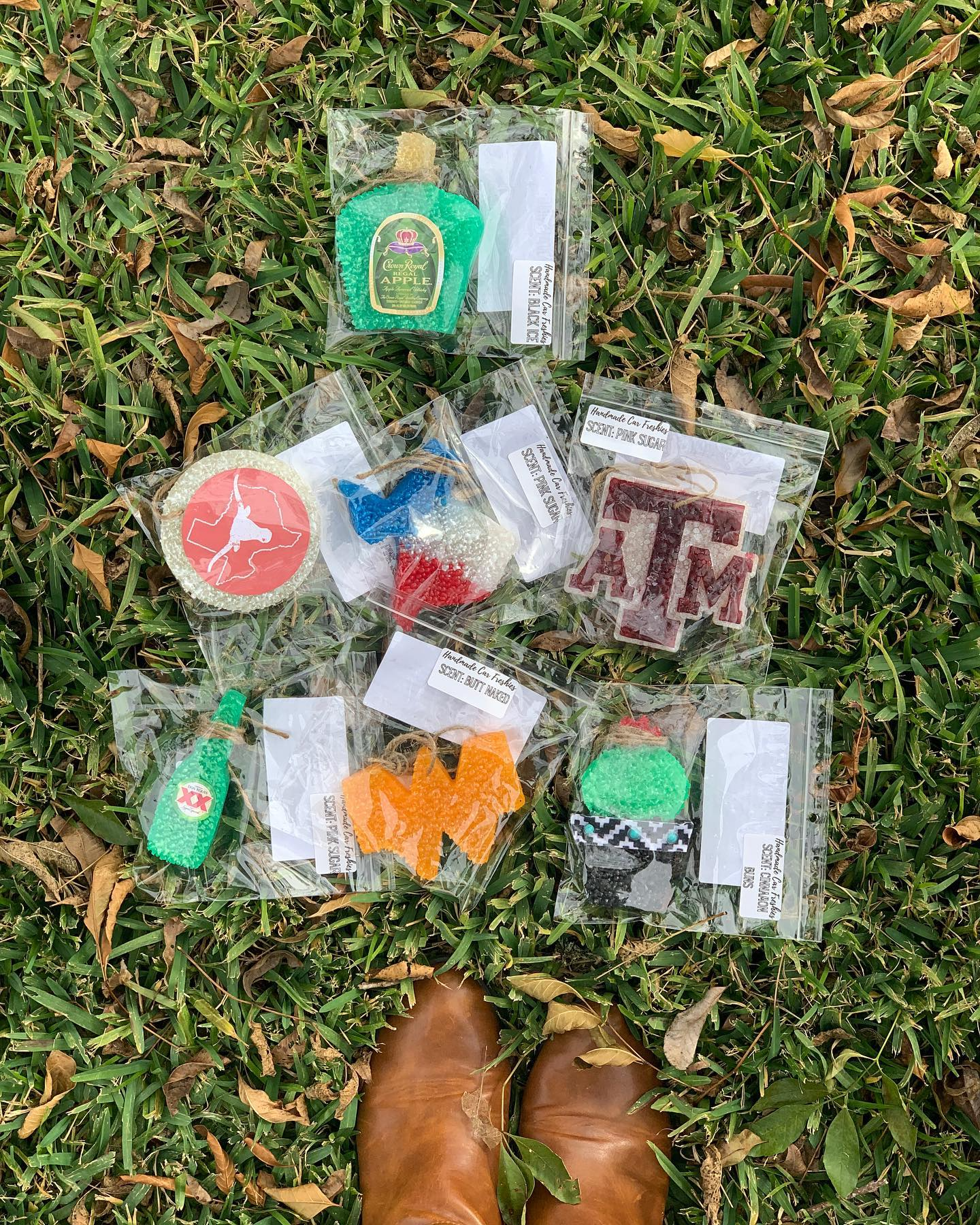 Assorted small packaged items laid on grass, with two brown shoes at the bottom edge.