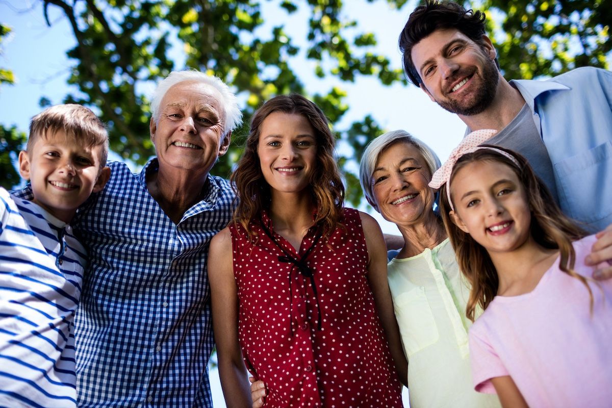 Smiling family group outdoors, leaning together against a blue sky background