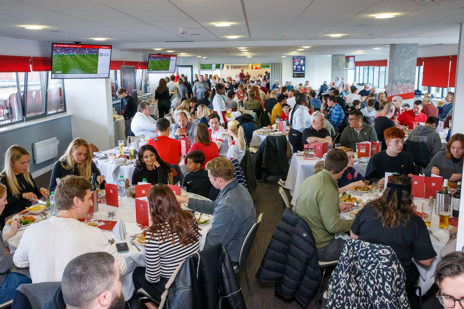 Crowded cafeteria with people seated at tables eating and talking in a bright, red-accented room