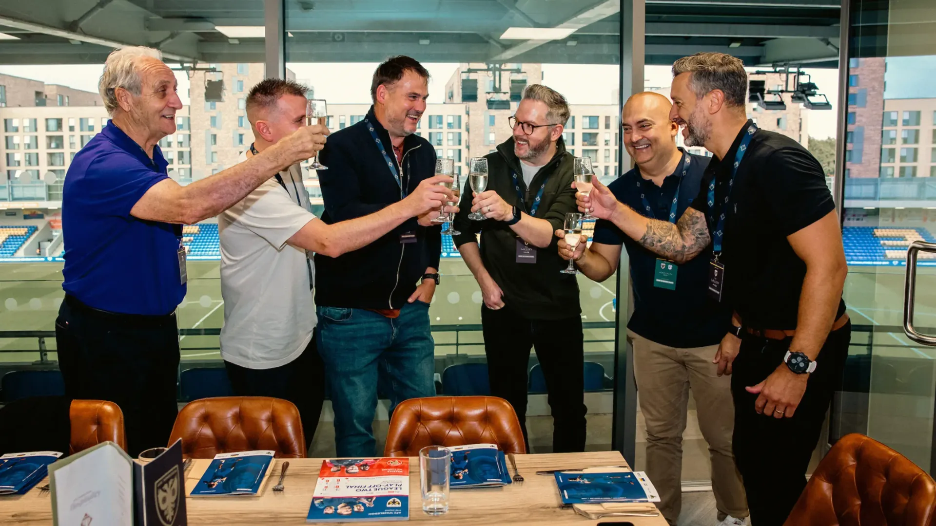 Five men standing around a table in an office, smiling and toasting drinks in celebration