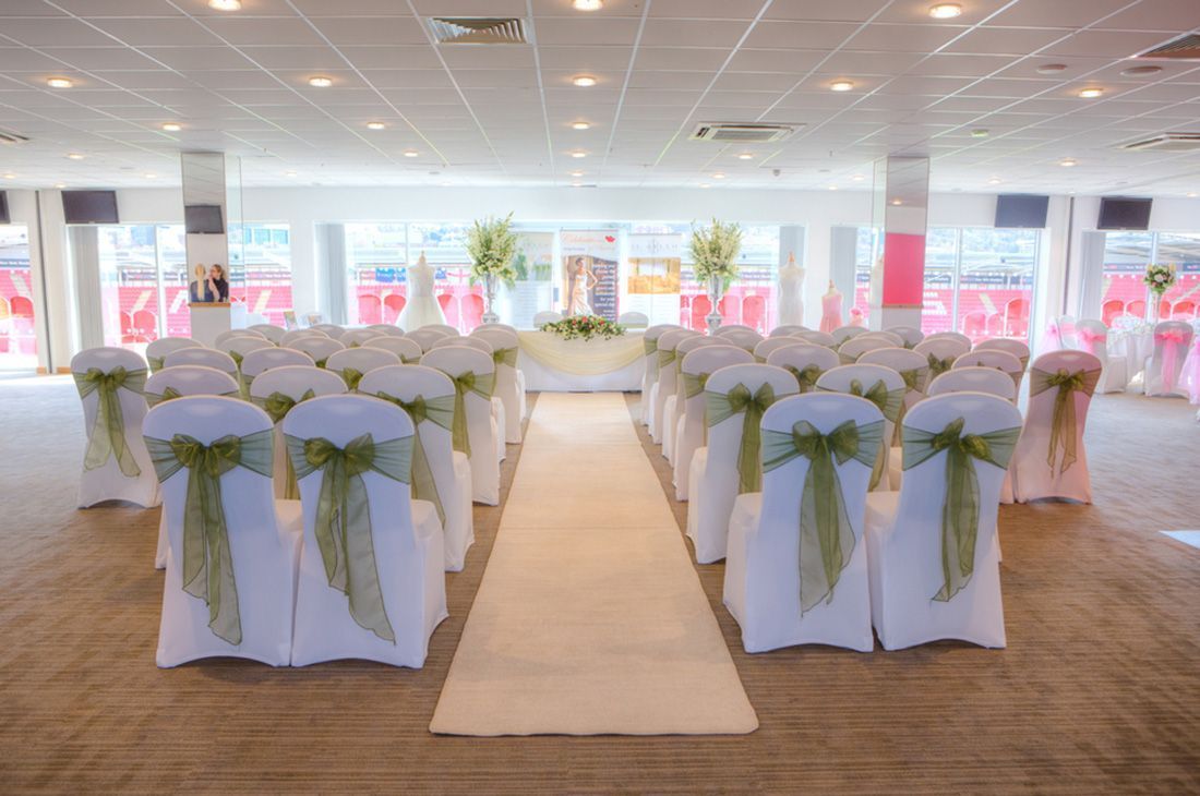 Elegant wedding reception room with white chairs, green bows, and a central aisle leading to tables.