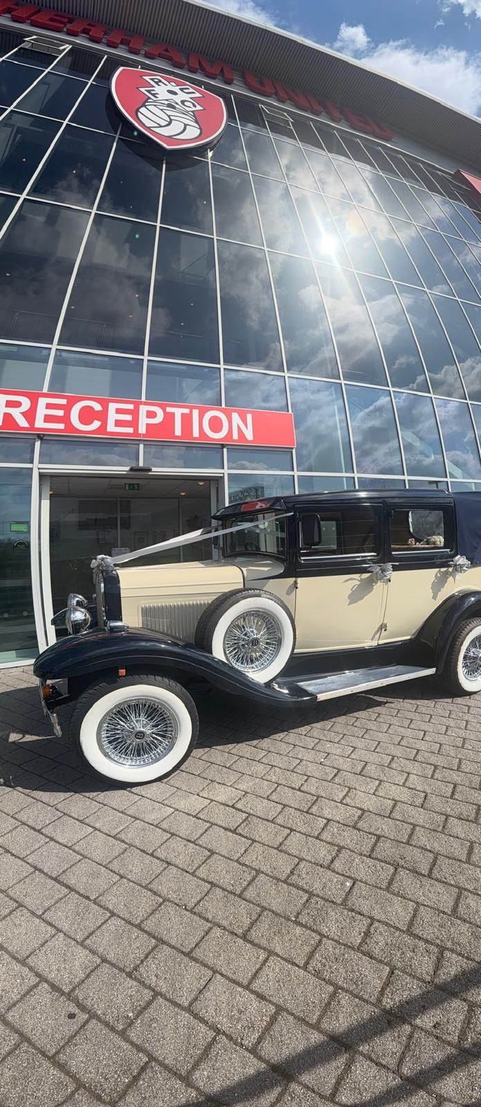 Vintage cream car parked outside a glass-fronted reception building with a red “RECEPTION” sign.
