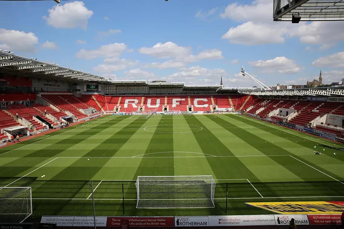 Empty football stadium with red and white seats and a green striped pitch under a blue sky