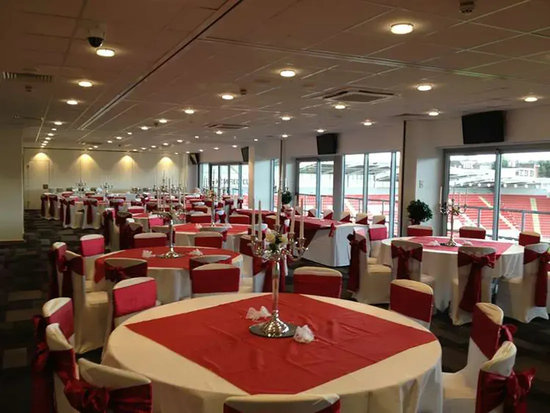 Restaurant dining room with red tablecloths, set tables, and large windows overlooking parked cars.