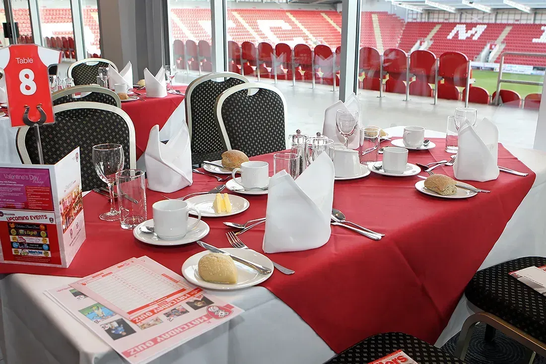 Red-draped dining tables set for a banquet with white chairs and tableware in a tented event space